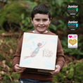 Load image into Gallery viewer, A young boy smiling while holding a My Forever Tooth Fairy Gift Set - Boy Version. The photo is taken outdoors in front of a blurred green background, with award badges shown on the right side.
