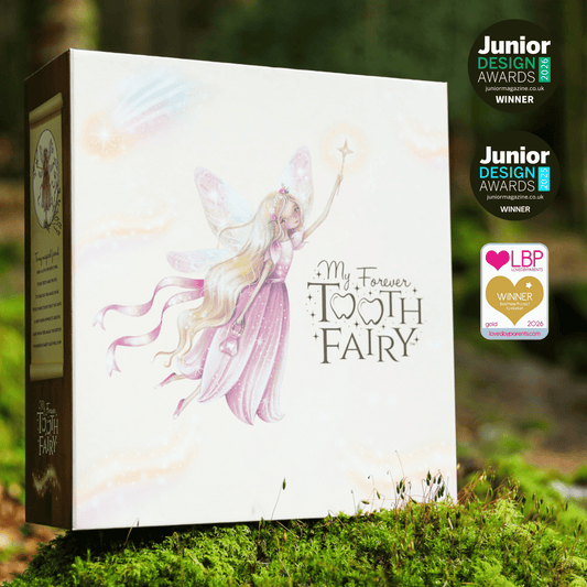 A boxed product titled "My Forever Tooth Fairy" stands outdoors on moss in a forest setting. The front of the box shows a pastel illustration of a fairy with long blonde hair and pink wings, with award badges shown on the right side of the image.